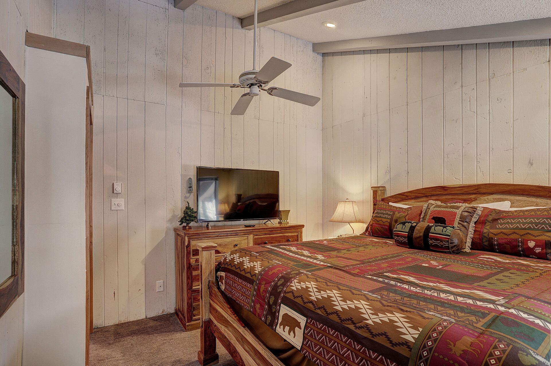 A bedroom with a wooden bed, a television on a wooden dresser, and a ceiling fan.
