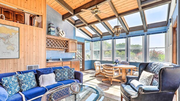 Une pièce spacieuse avec un grand plafond en bois, une véranda vitrée, un canapé bleu, un fauteuil en cuir et une table à manger avec des chaises.