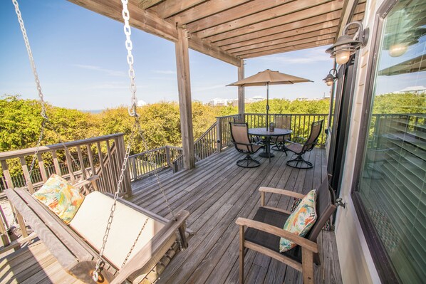 A wooden deck with a swing chair, a table with chairs, and an umbrella.