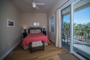 Une chambre à coucher comprenant un lit, deux tables de chevet, un ventilateur de plafond et une vue sur l’extérieur grâce à une porte-fenêtre coulissante.