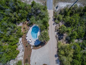 An aerial view of a private property with a swimming pool surrounded by lush greenery and a paved walkway.