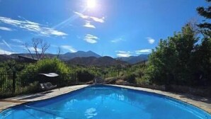 Une piscine bordée de pierres, entourée de verdure et avec des montagnes en toile de fond.