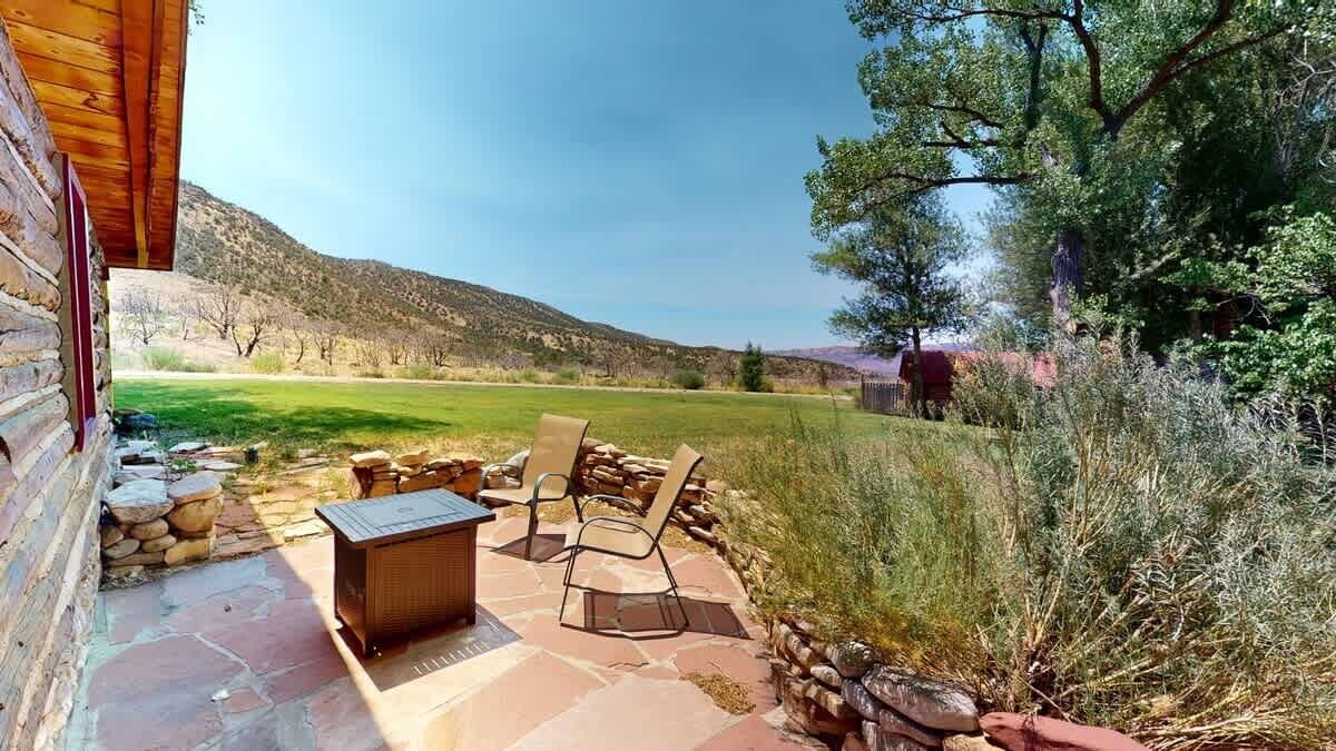 A patio with stone flooring, a wooden table, and two chairs.