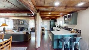A rustic interior with a stone fireplace, wooden ceiling beams, a kitchen with bar stools, and a dining area with a table and chairs. - Pack Creek - Road House (Moab)