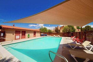 A swimming pool with lounge chairs and a shaded area, surrounded by buildings. - Sunset View - 3234 (Moab)