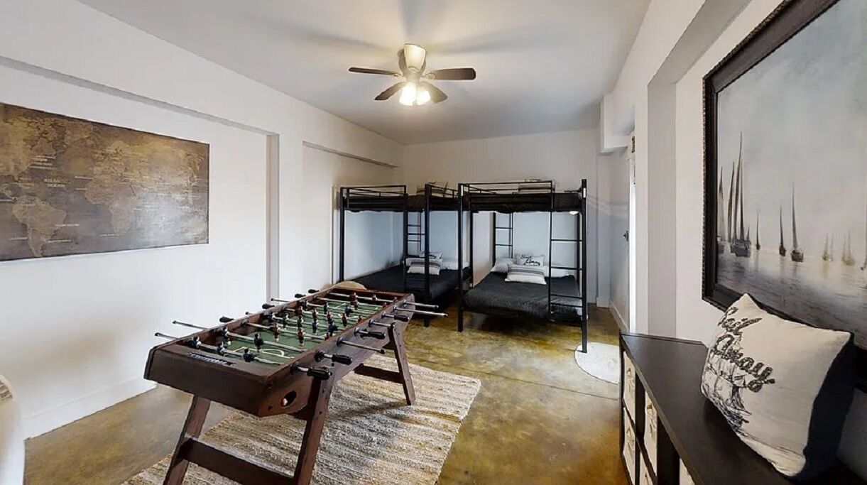 A room with bunk beds, a foosball table, a world map, and a painting of sailboats.