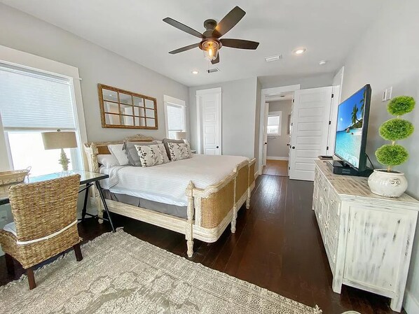 A bedroom with a bed, a ceiling fan, a TV, a dresser, and a window.