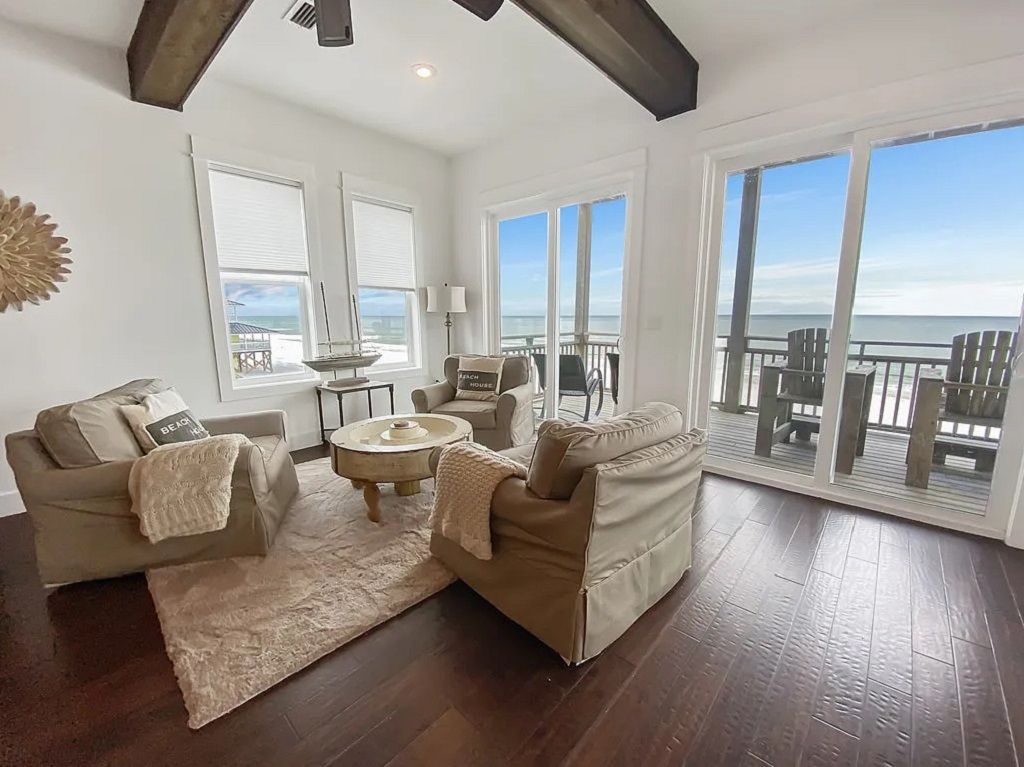 A spacious living room with a large window overlooking the ocean, furnished with a sofa, armchairs, and a coffee table.