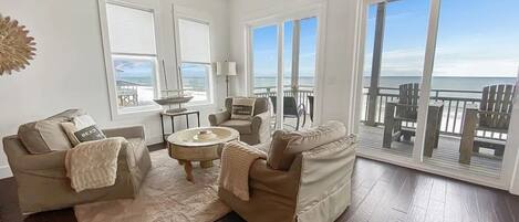 A spacious living room with a large window overlooking the ocean, furnished with a sofa, armchairs, and a coffee table.