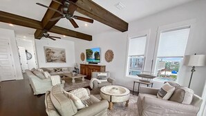 Ein geräumiges Wohnzimmer mit Deckenventilator, großem Fenster mit Jalousien, Fernseher und Kamin.