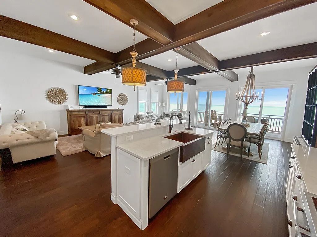 A spacious living area with a large island, wooden beams, a dining area, and a view of the ocean.