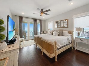 Un'ampia camera da letto con un letto grande, un ventilatore a soffitto, una televisione e un balcone vista mare.