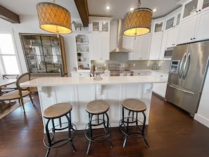 A kitchen with white cabinets, a stainless steel refrigerator, a large island with stools, and pendant lighting.