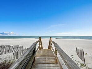 Una passerella di legno conduce a una spiaggia sabbiosa sotto un cielo azzurro e limpido.