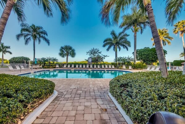 A pool surrounded by palm trees and a paved walkway.