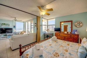 A hotel room with a bed, a TV, a sofa, a dresser, and a balcony with a view.