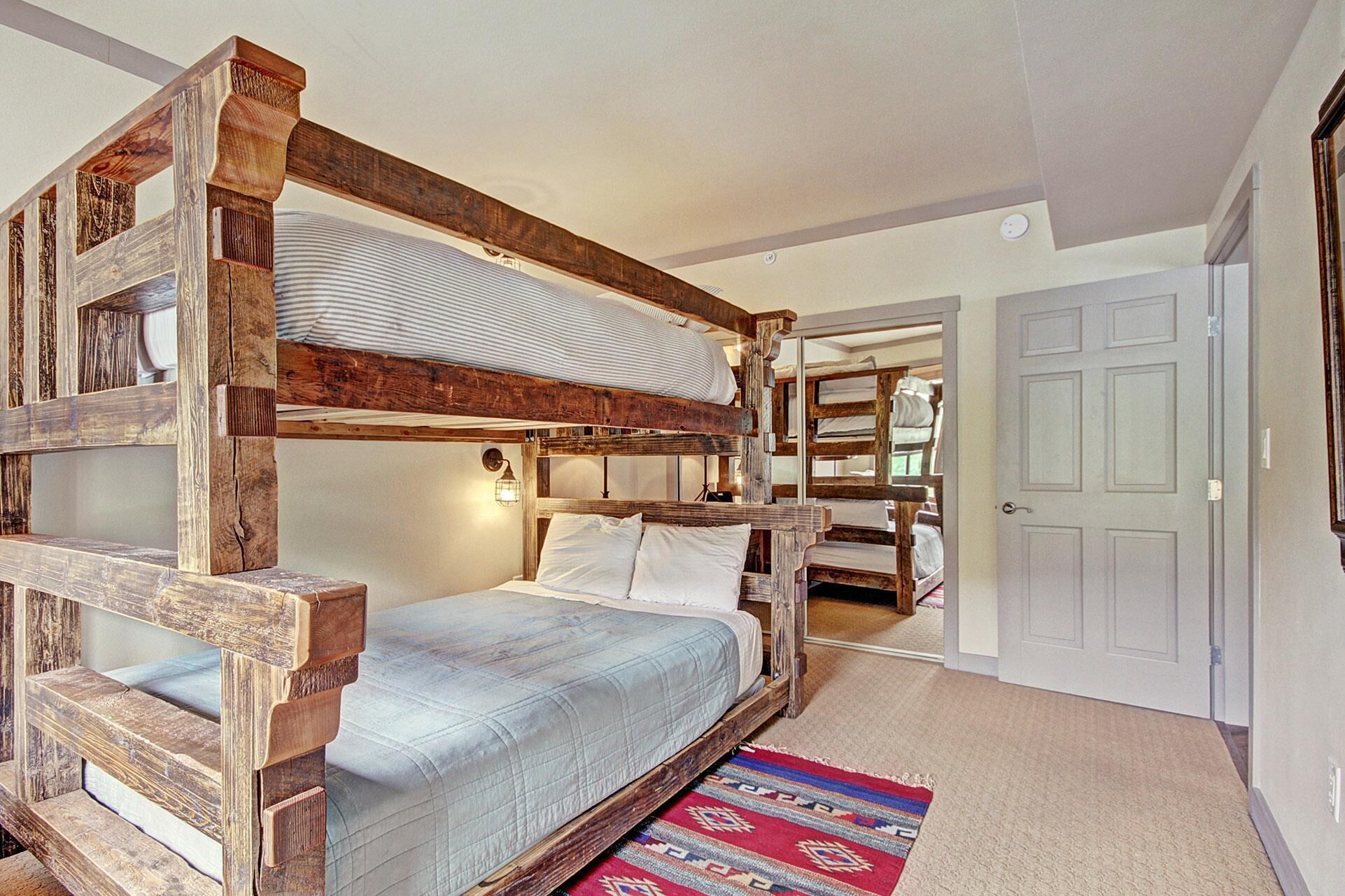A bunk bed room with a wooden frame, a single bed, and a red patterned rug.