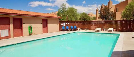 A swimming pool with lounge chairs and a wooden fence.