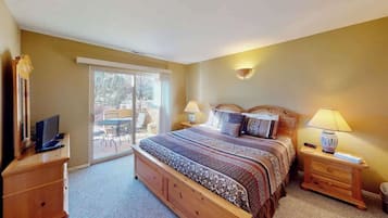 A bedroom with a bed, bedside tables, a lamp, a television, and a sliding glass door leading to an outdoor area.