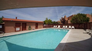 A swimming pool with a wooden deck, lounge chairs, and a building with a red roof.
