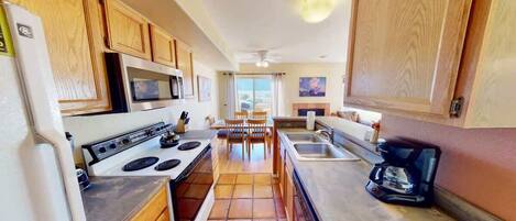 A compact kitchen with wooden cabinets, a microwave, stove, and a coffee maker.
