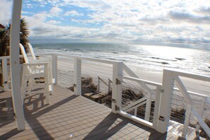 A wooden deck with a white railing overlooking the beach.
