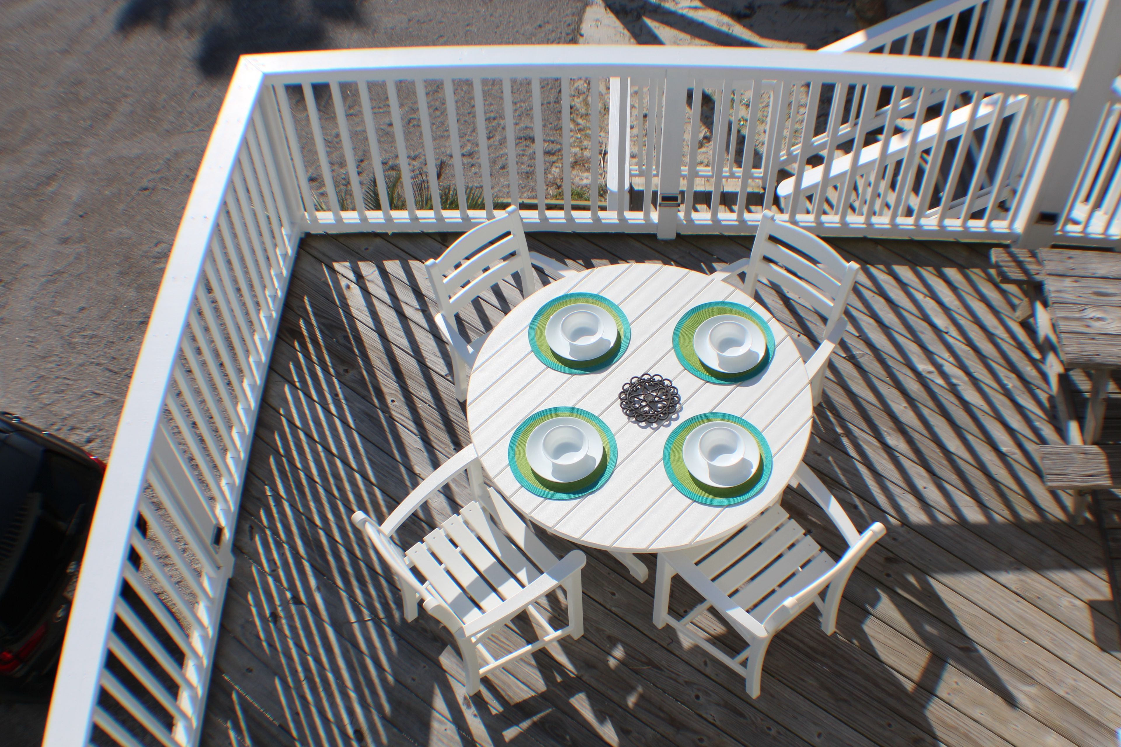 A round table with four chairs, surrounded by a white railing on a wooden deck.