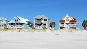 A row of beach houses with balconies, each with a different color, situated on a sandy beach with clear skies. - Beach Front, dog friendly, 20 steps to Beach! (Cape San Blas)