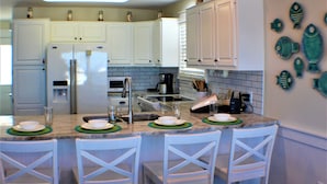A kitchen with white cabinets, a refrigerator, a sink, and a bar area with chairs. - Beach Front, dog friendly, 20 steps to Beach! (Cape San Blas)