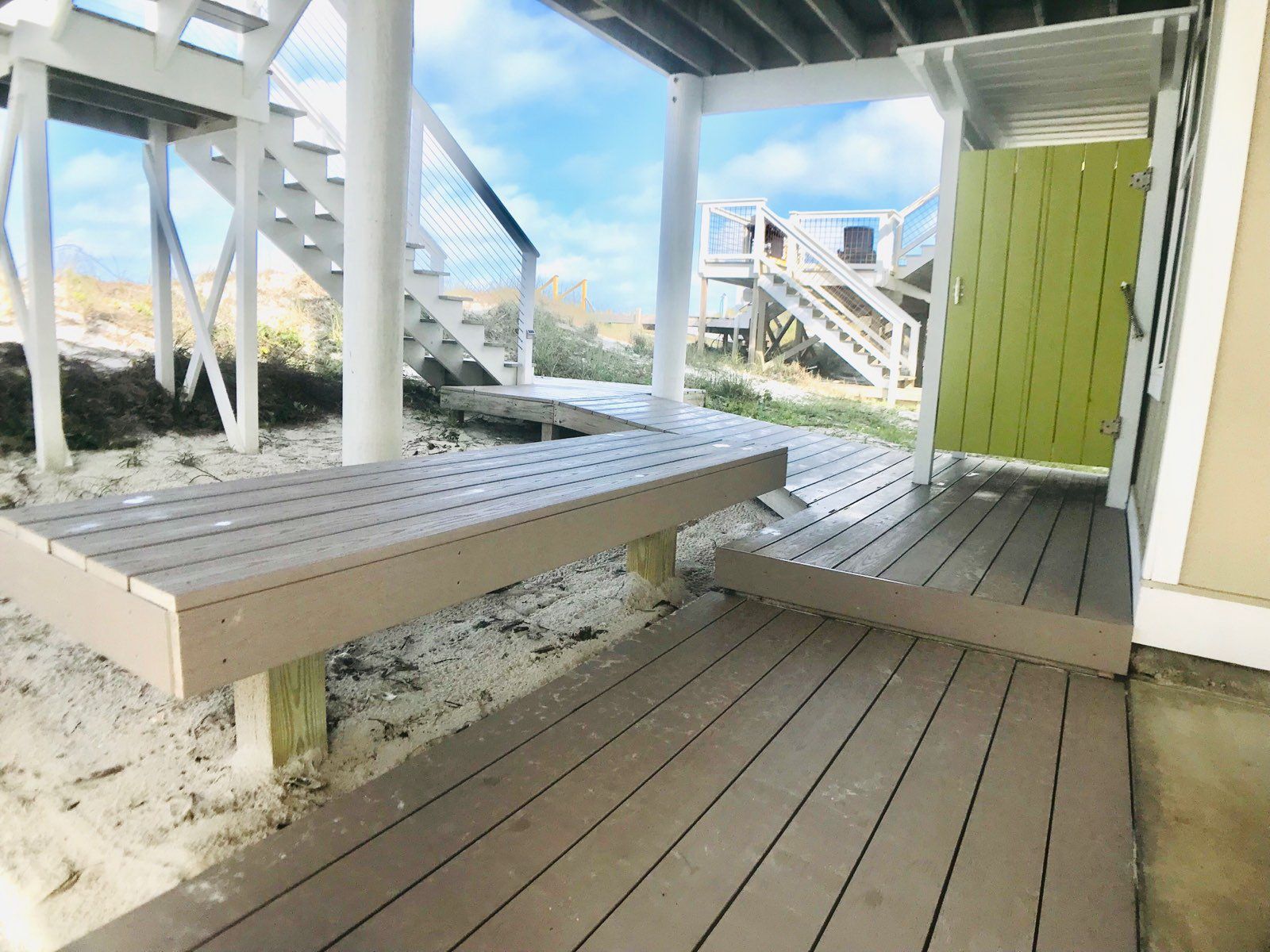 Una terraza de madera con un banco, pilares blancos y una puerta verde.