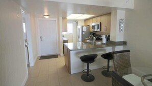 A modern kitchen with a central island, bar stools, and a microwave. - Carlos Pointe #531 Cozy Beachfront Condo (Fort Myers Beach)