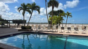 A swimming pool with lounge chairs and palm trees. - Carlos Pointe #531 Cozy Beachfront Condo (Fort Myers Beach)