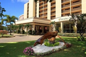 Un hôtel doté d’une façade moderne, d’une entrée centrale et d’un jardin aménagé avec une sculpture.