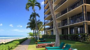 A beachfront hotel with multiple balconies, a pathway leading to the beach, and lounge chairs with green cushions. - Time to Spoil Yourself!  Deluxe Ocean Front and Steps to N. Kaanapali Beach ~ (Lahaina)
