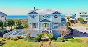 A two-story house with a balcony, a front yard with a small pool, and a view of the ocean.