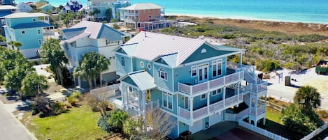 A large, multi-story beachfront property with a prominent balcony and a view of the ocean.