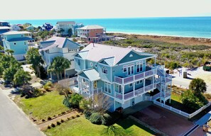 A large, multi-story beachfront property with a prominent balcony and a view of the ocean.