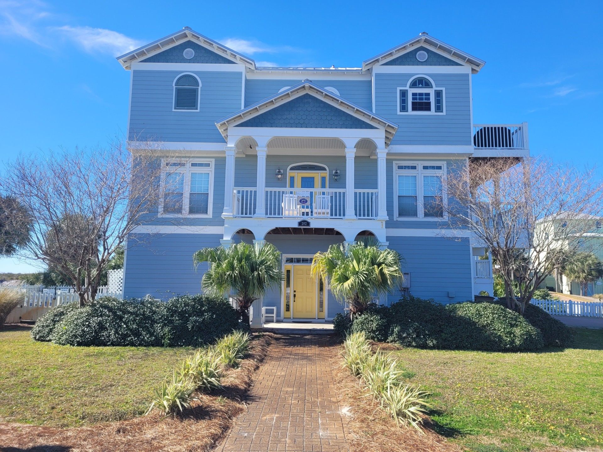 A two-story house with a central porch, a yellow front door, and a brick pathway leading to the entrance.