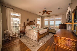 A spacious bedroom with a large bed, a wooden desk, and a ceiling fan.
