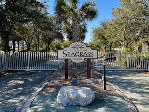 A sign welcoming visitors to Seagrass, a private community for Seagrass residents only, with a white picket fence and a large rock in the foreground.