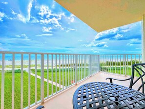 Ein Balkon mit Blick auf den Strand, einem Metalltisch und einem weißen Geländer.