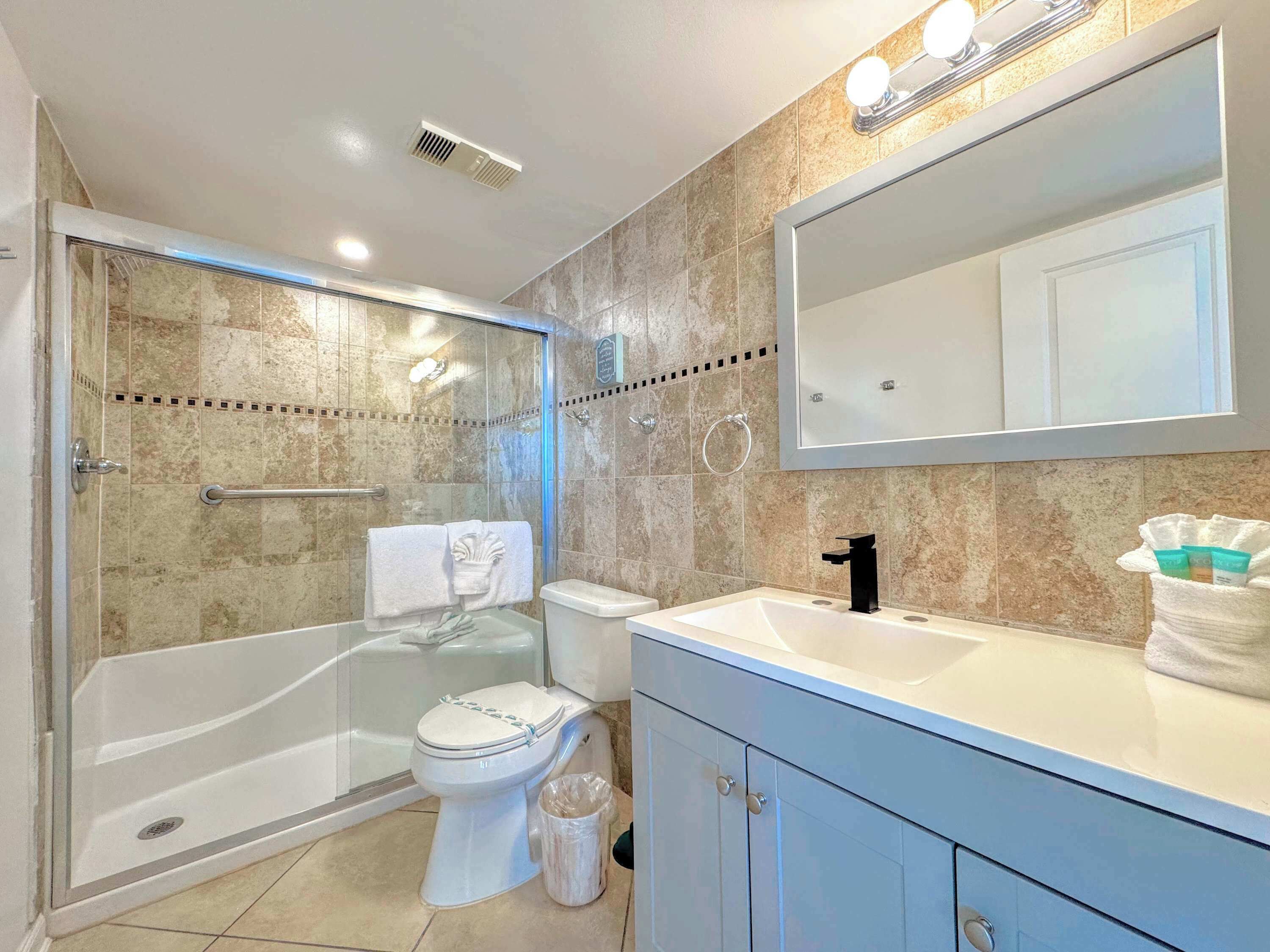 A modern bathroom with a glass-enclosed shower, a toilet, a sink with a mirror above, and a towel rack.