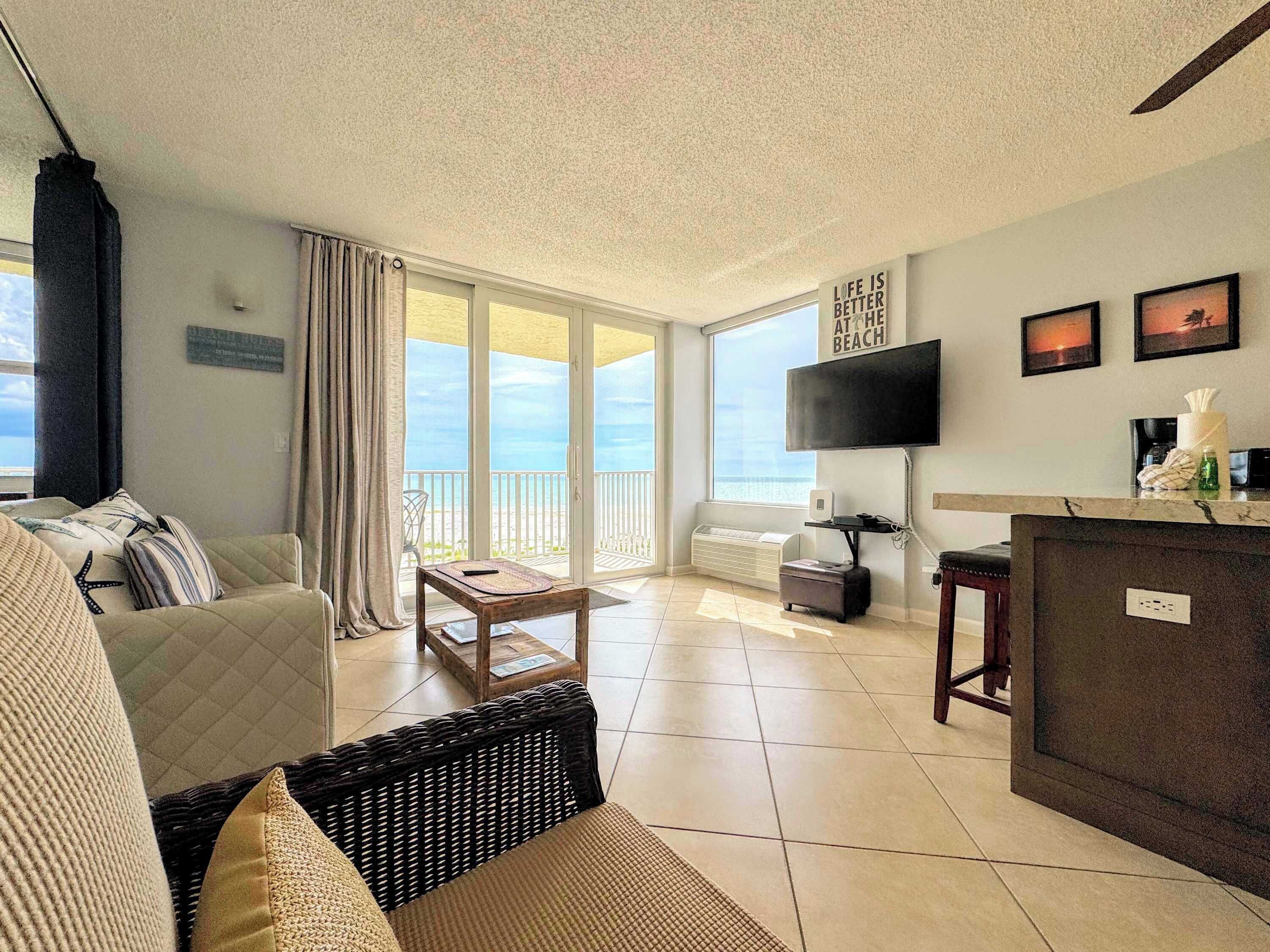 Une chambre d’hôtel avec un balcon, un canapé, une table basse, une télévision et un bureau avec un ordinateur.