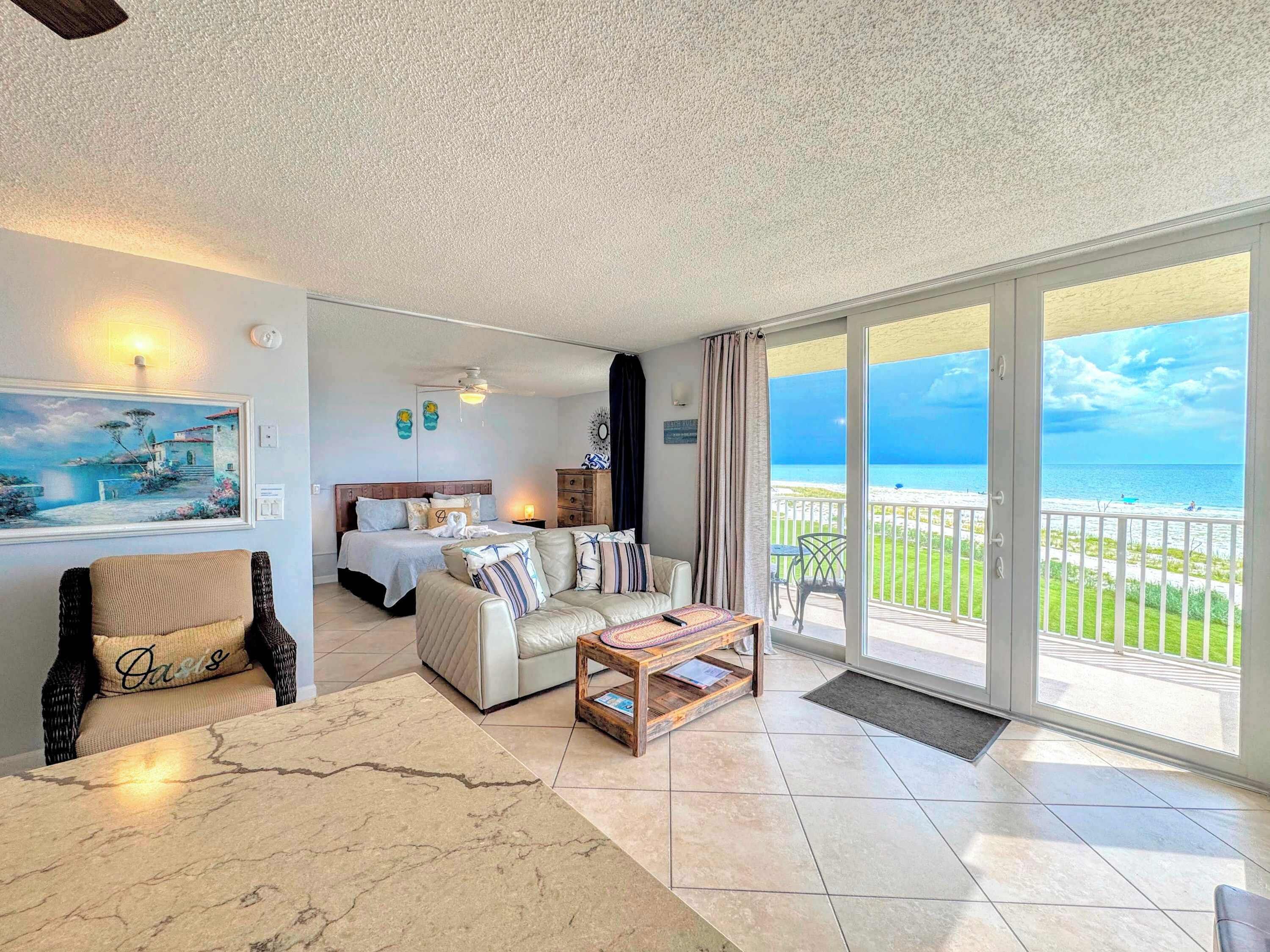 A hotel room with a bed, a sofa, a coffee table, and a balcony with a view of the sea.
