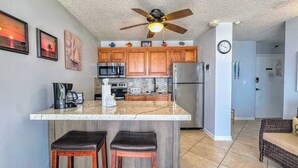 A modern kitchen with wooden cabinets, a central island, stainless steel appliances, and a ceiling fan. - Estero Beach & Tennis Club #203B Beachfront Condo (Fort Myers Beach)