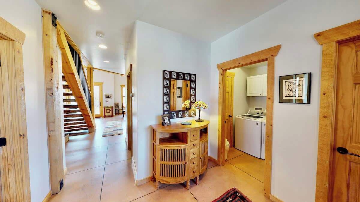A hallway with a wooden staircase, a wooden cabinet, and a kitchen area visible through an open door.
