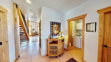 A hallway with a wooden staircase, a wooden cabinet, and a kitchen area visible through an open door.