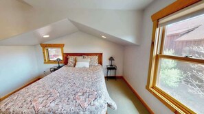 Ein Schlafzimmer mit einem großen Bett, einem Fenster, einem Nachttisch und einer Lampe.