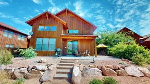 A two-story wooden cabin with a covered patio, large windows, and a satellite dish. - Rim View Retreat - 14, Luxurious Stand-Alone 3 Be (Moab)