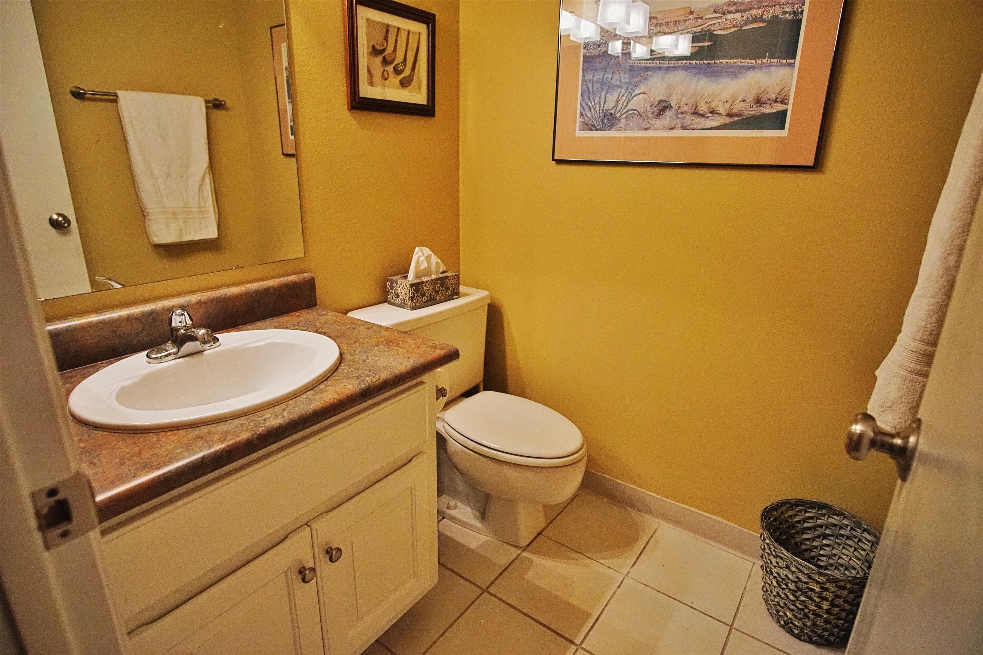 Casa de banho com lavatório, sanita e um quadro emoldurado na parede.